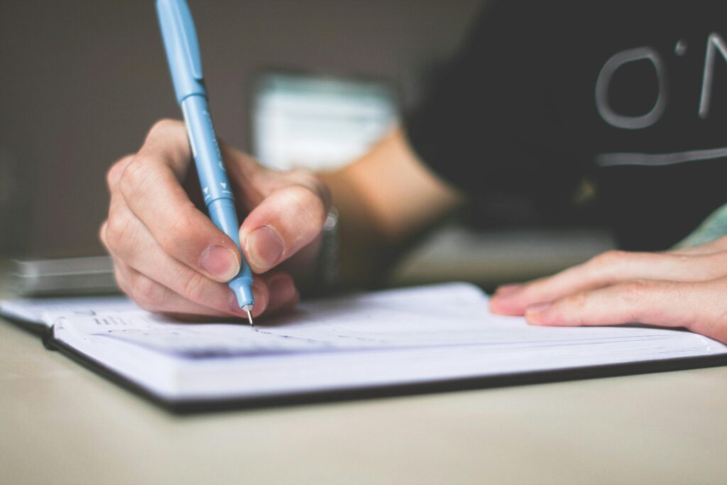 pexels-photo-210661-210661 Person Holding Blue Ballpoint Pen Writing in Notebook